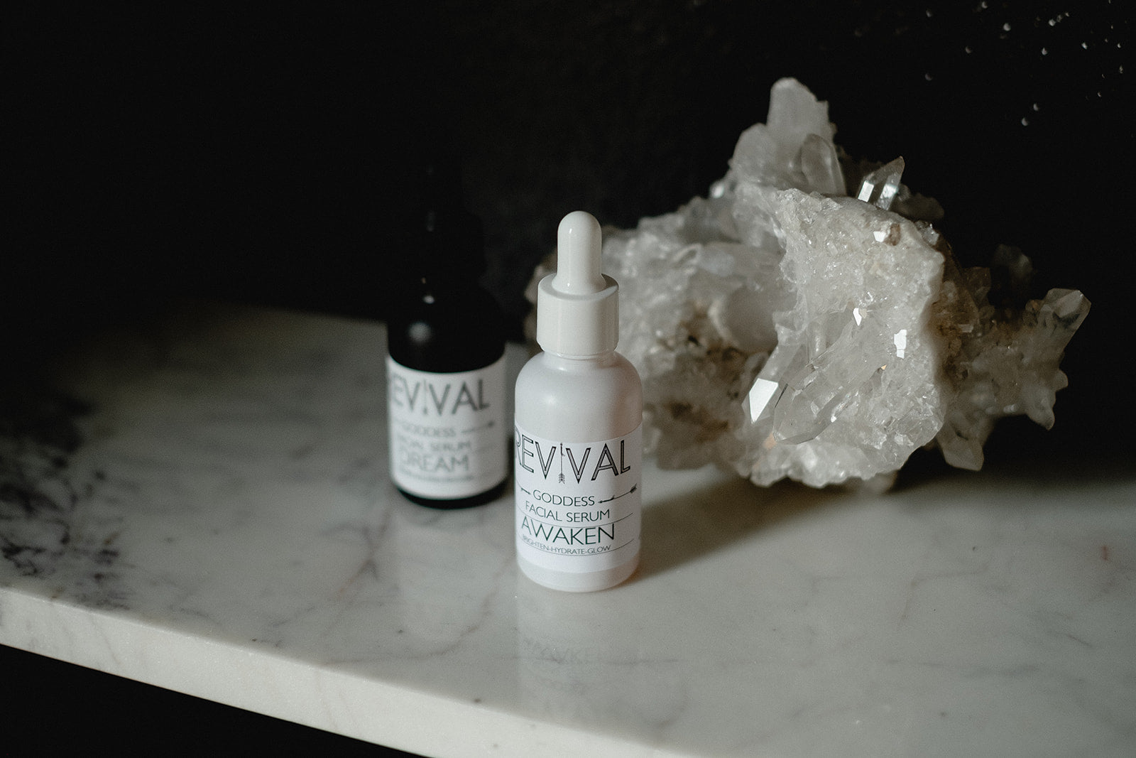 Two skincare products labeled 'REVIVAL' on a marble surface with a dark background.