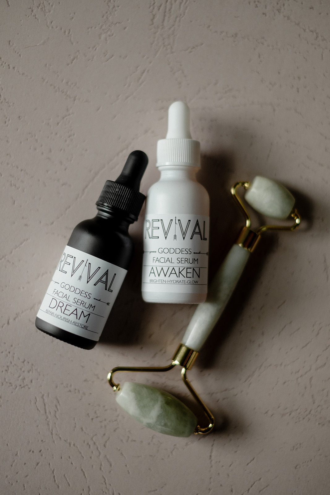 Three skincare products with 'REVIVAL' branding on a textured beige surface.