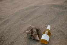 Bottle of Revival Covet Body Oil on sand with Quartz Stone