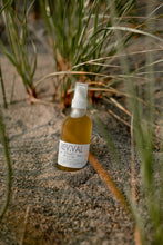 Revival bottle of Covet Body Oil on a sandy surface with grasses