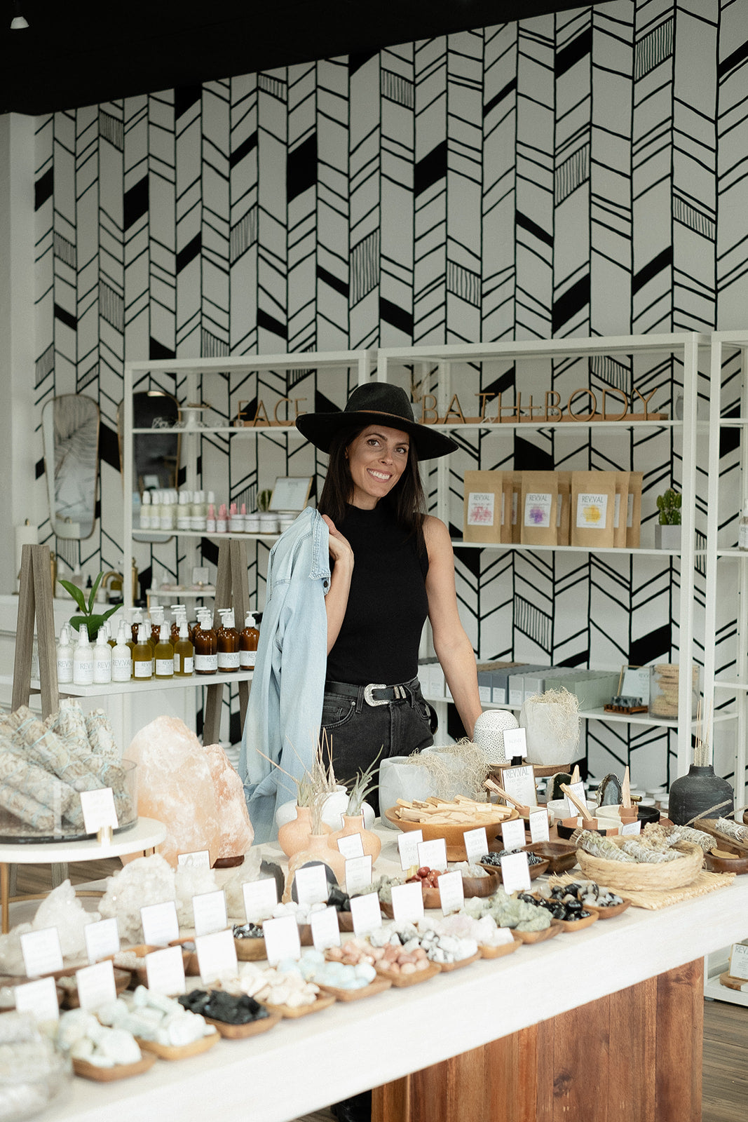 Woman standing behind a counter with various items in a store setting.