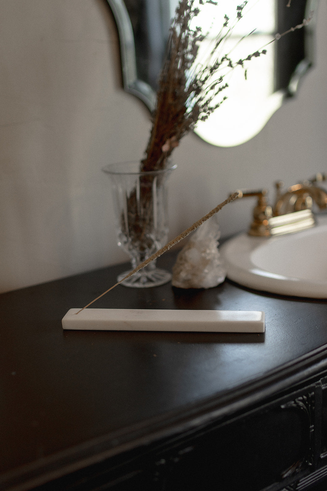 Marble incense holder on a dark wooden surface with a vase and decorative elements in the background.