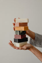 Stack of colorful Revival Body Care soap bars held in a hand against a neutral background