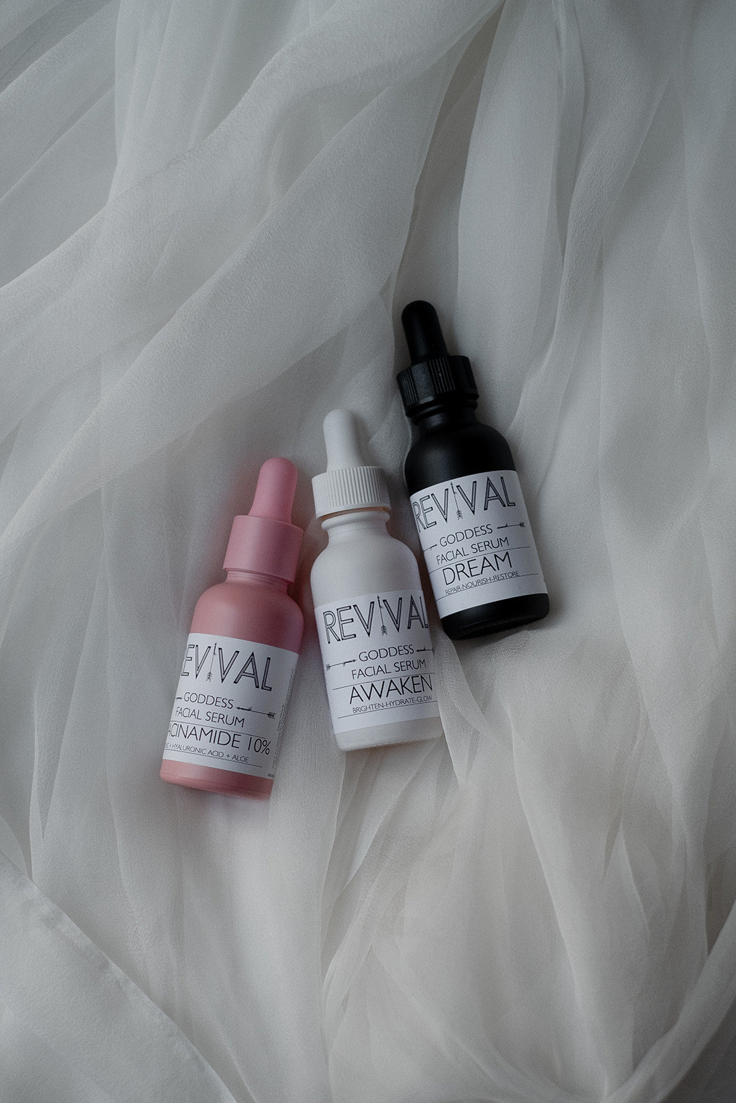 Three skincare bottles labeled 'REVIVAL' on a white fabric background