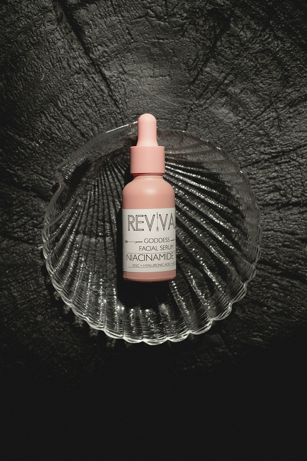 Pink facial serum bottle labeled 'REVIVAL' on a dark textured background