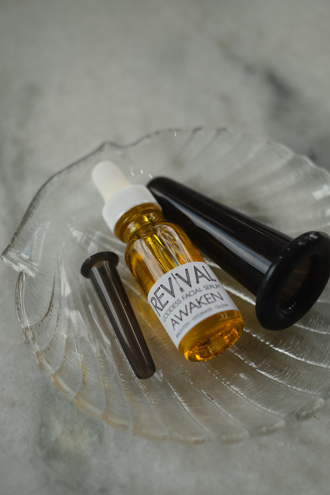 The image shows a Revival facial cupping kit which includes two silicone cups in different sizes and a small bottle of facial oil, all placed on a glass dish.