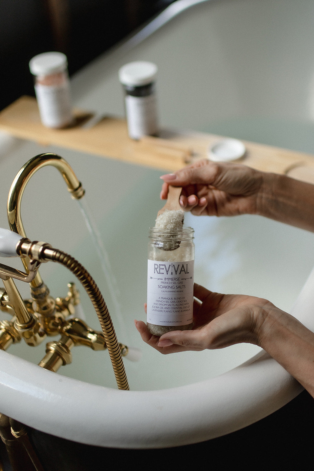 Person holding a 'Revival' product over a bathtub with bottles on a shelf.