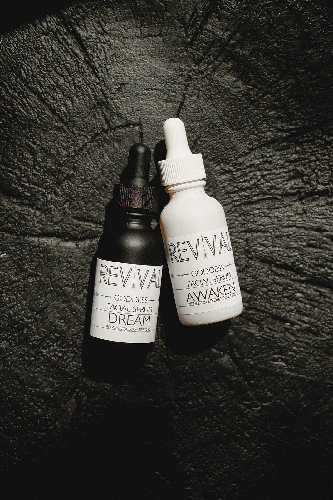Two skincare serum bottles labeled 'Revival' on a dark textured surface