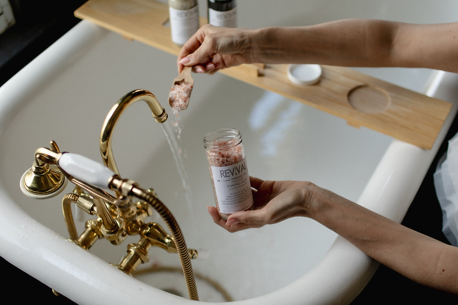 Person holding a jar labeled 'Revival' over a sink with gold fixtures.