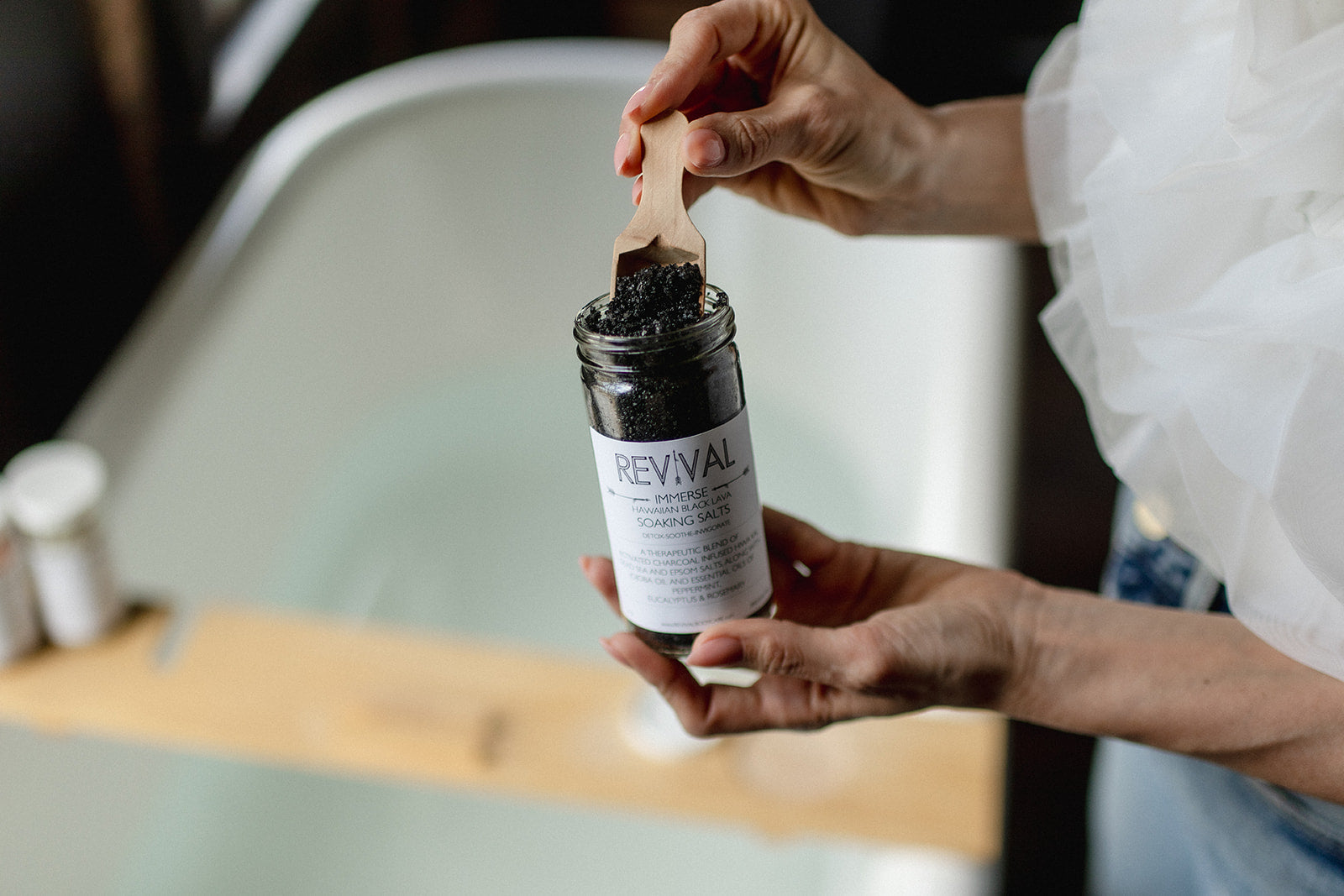 Person holding a skincare product labeled 'Revival' with a wooden applicator.