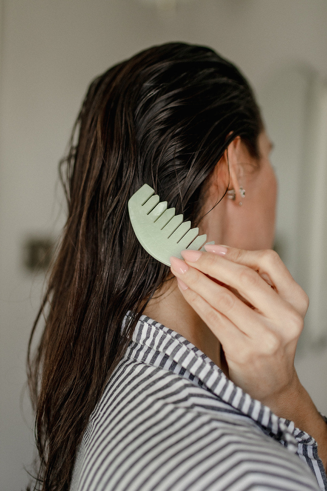 Person using a green comb in their hair with a neutral background