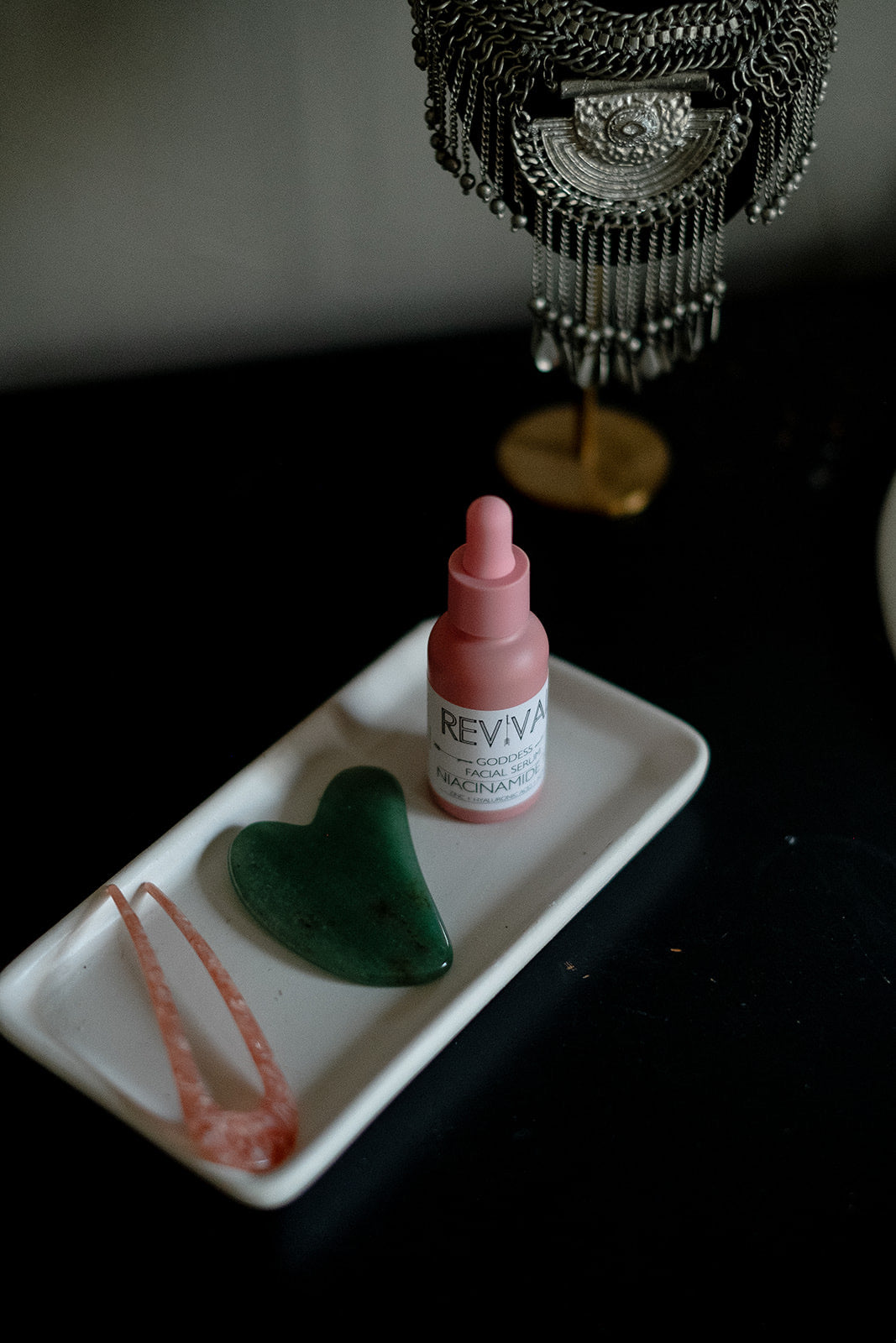 A bottle of niacinamide serum on a white tray with a heart-shaped locket and a pink necklace, placed on a wooden surface.