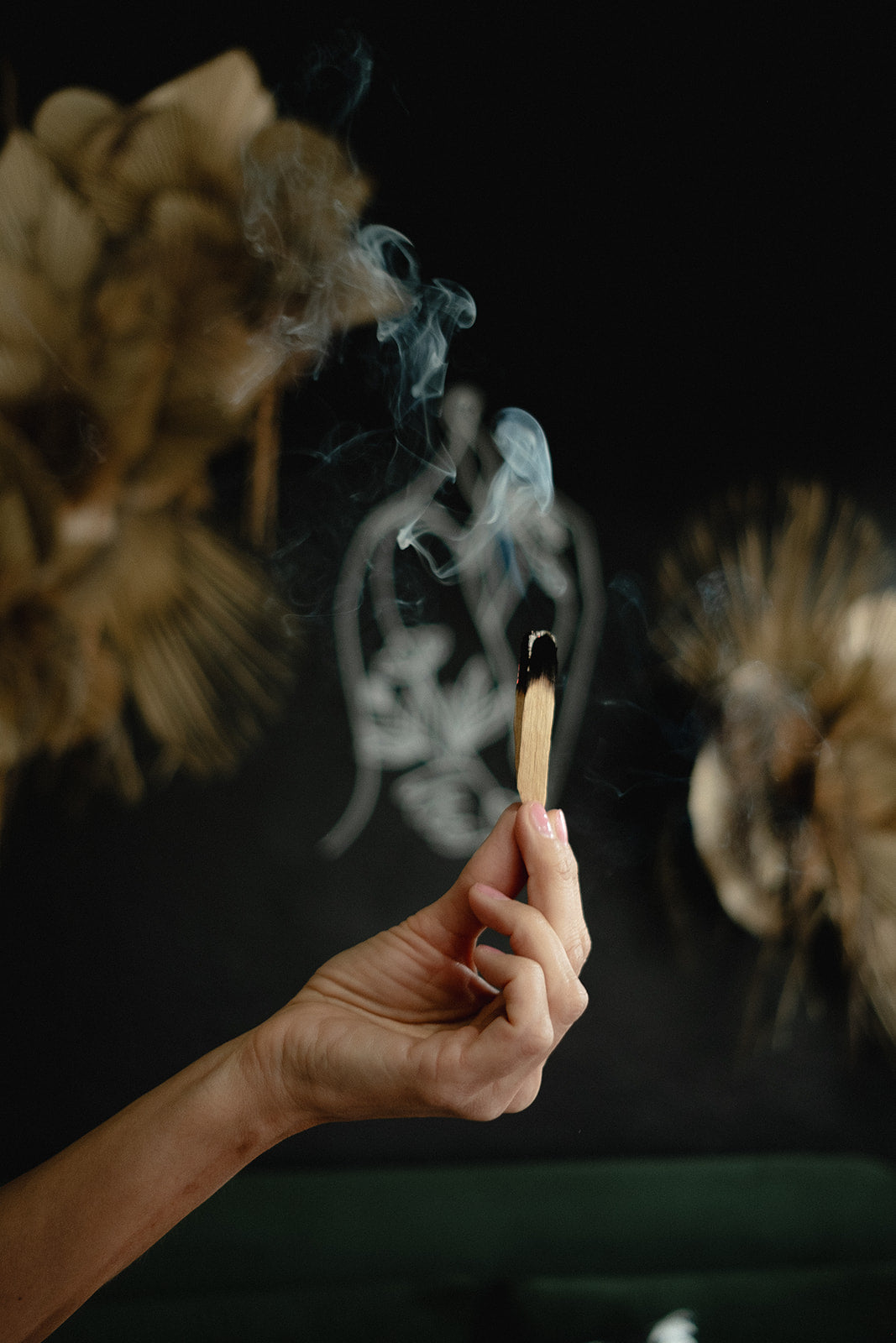 Hand holding a smoking Palo Santo stick with decorative elements in the background