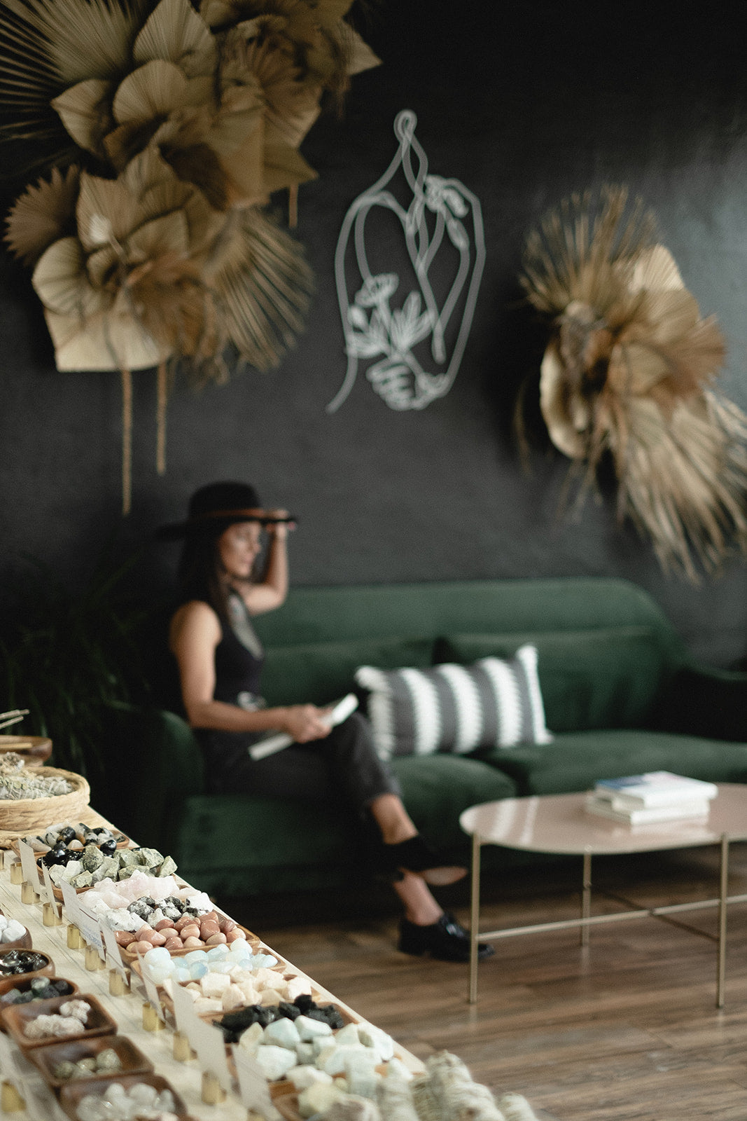 Woman sitting on a green couch in a stylish room with decorative elements and plants.