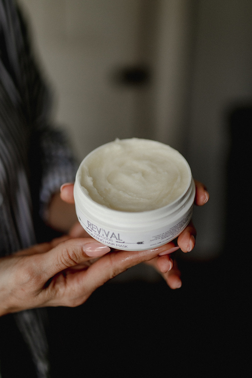 Person holding a jar Revival Lush Locks with a blurred background