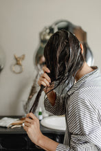 Person applying Revival Hair Mask to hair in a bathroom sink with a mirror and towel rack visible.