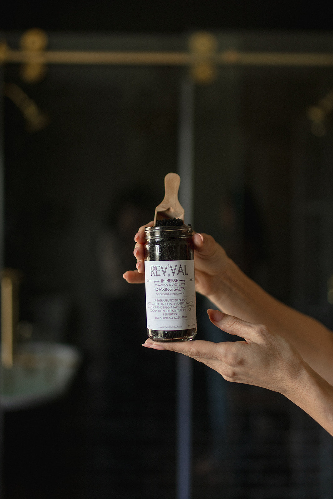 Hand holding a bottle labeled 'REVIVAL' against a dark background