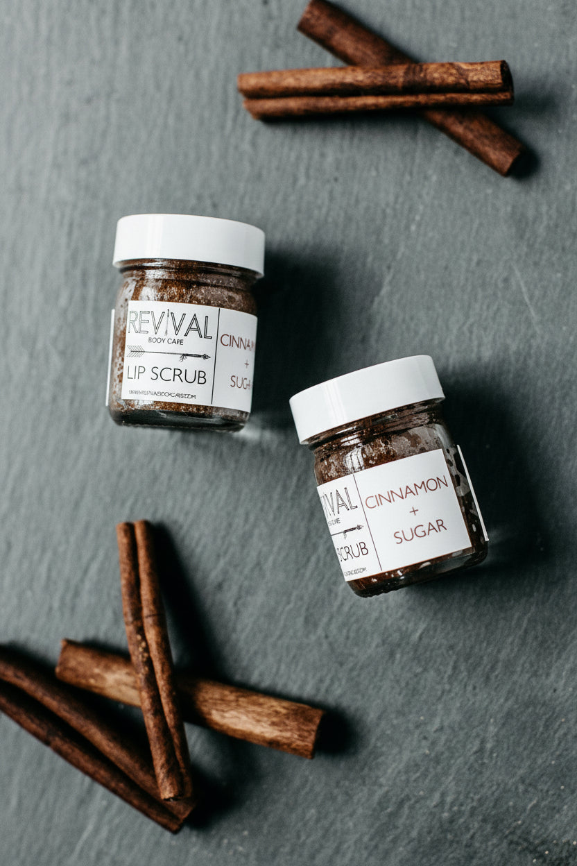 Revival Cinnamon Sugar Lip Scrubs on grey surface with cinnamon sticks