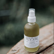  'REVIVAL COVET BODY OIL' placed on a wooden surface.