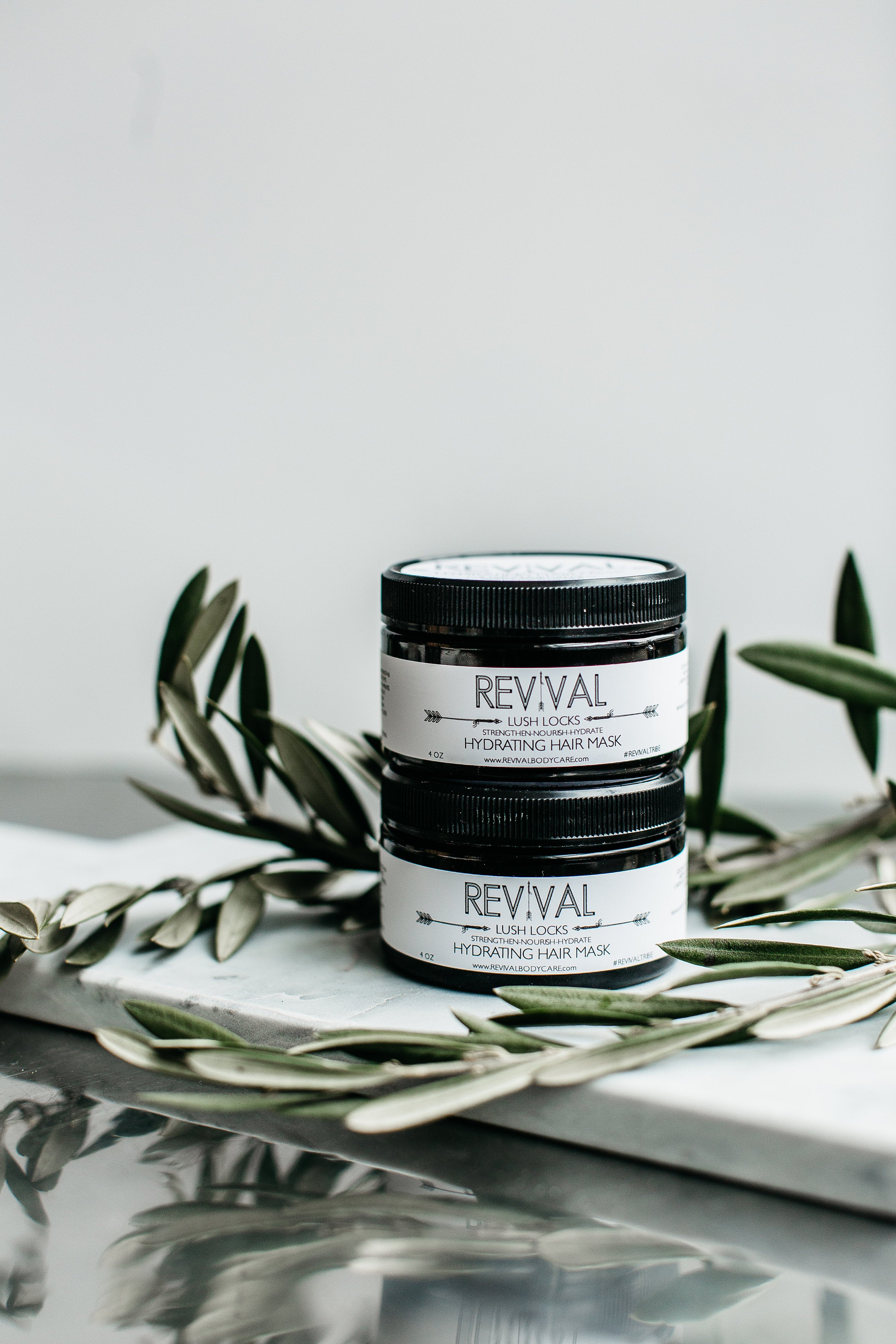 A jar of LUSH LOCKS HYDRATING HAIR MASK with a label that reads 'REVIVAL'. The jar is placed on a surface with a leafy decoration in the background.