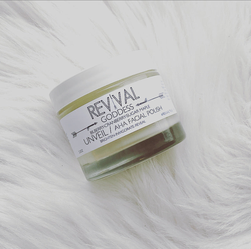 A jar of UNVEIL AHA FACIAL POLISH by Revival Body Care, placed on a white furry surface.