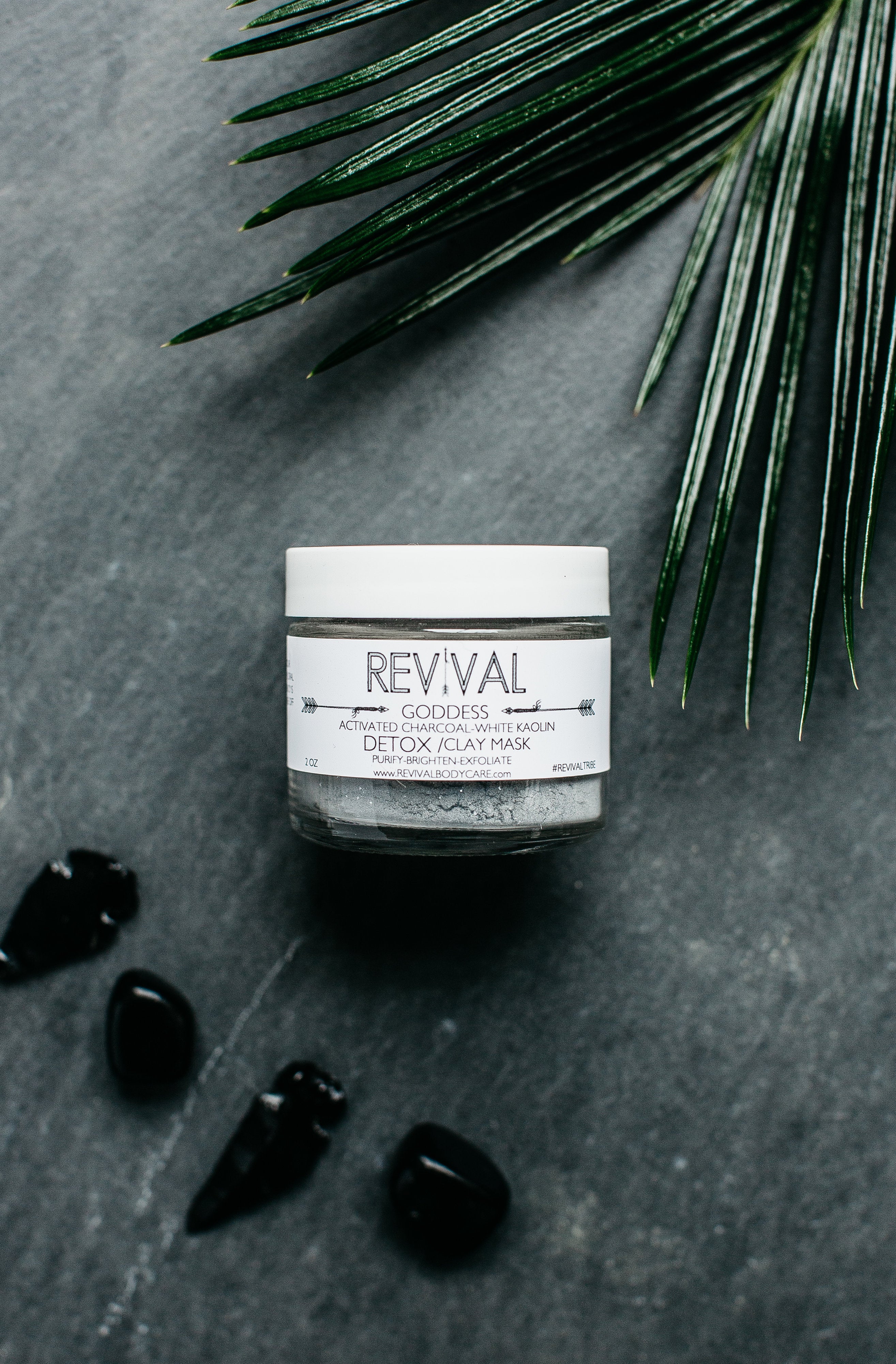 A jar of GODDESS CLAY MASK - DETOX with activated charcoal and a leaf in the background, indicating a natural and vegan skincare product.
