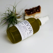 Bottle of Revival Body Care Covet Body Oil on White background with gemstone and plant 
