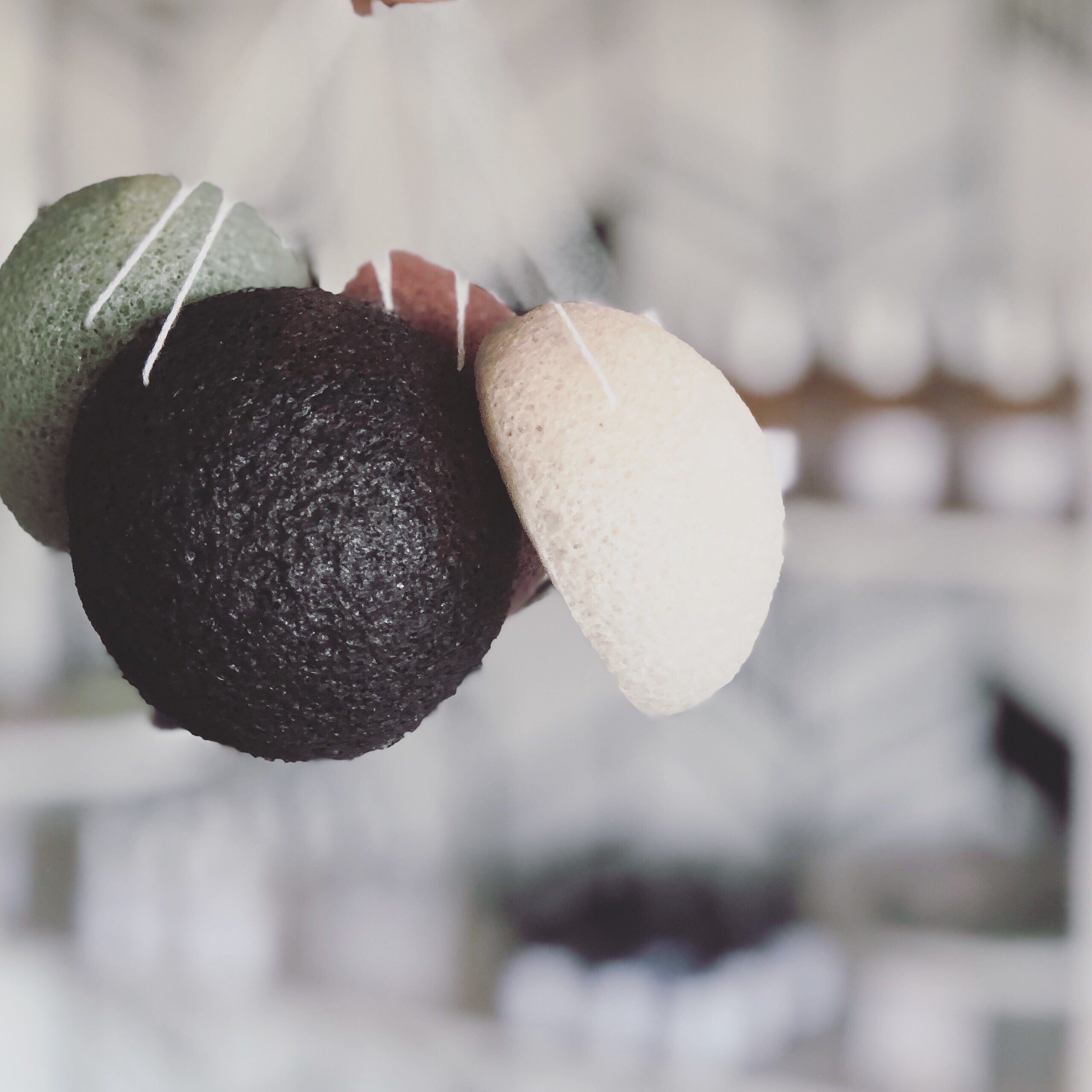 A selection of Konjac sponges hanging, showing different colors including black, green, beige, and pink.