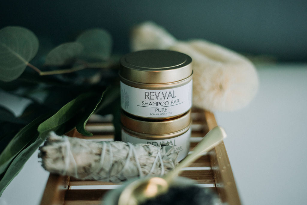 A shampoo and conditioner bar from Revival, placed on a wooden surface with green leaves in the background, indicating it is a natural hair care product.